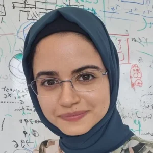 Sarah Barendswaard, research engineer, in glasses and a teal hijab, stands before a whiteboard with diagrams.